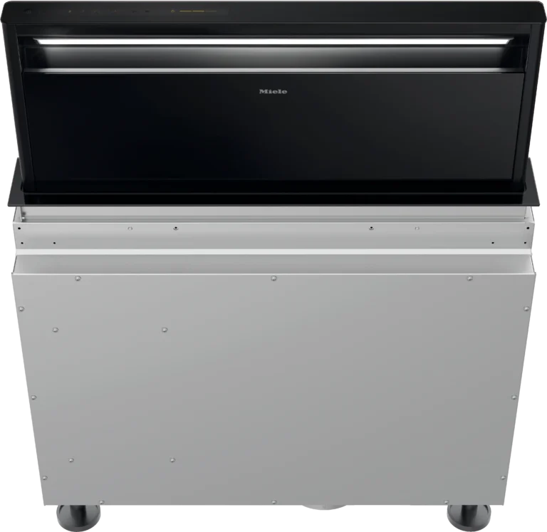 Zostupná ventilačná jednotka Miele s čiernou sklenenou čelnou stenou, čiastočne vysunutou z puzdra z ušľachtilej ocele.